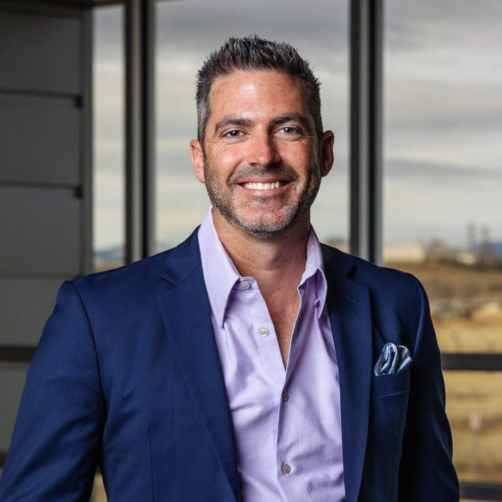 A man in a blue suit smiling in front of a window, representing Fann Contracting.