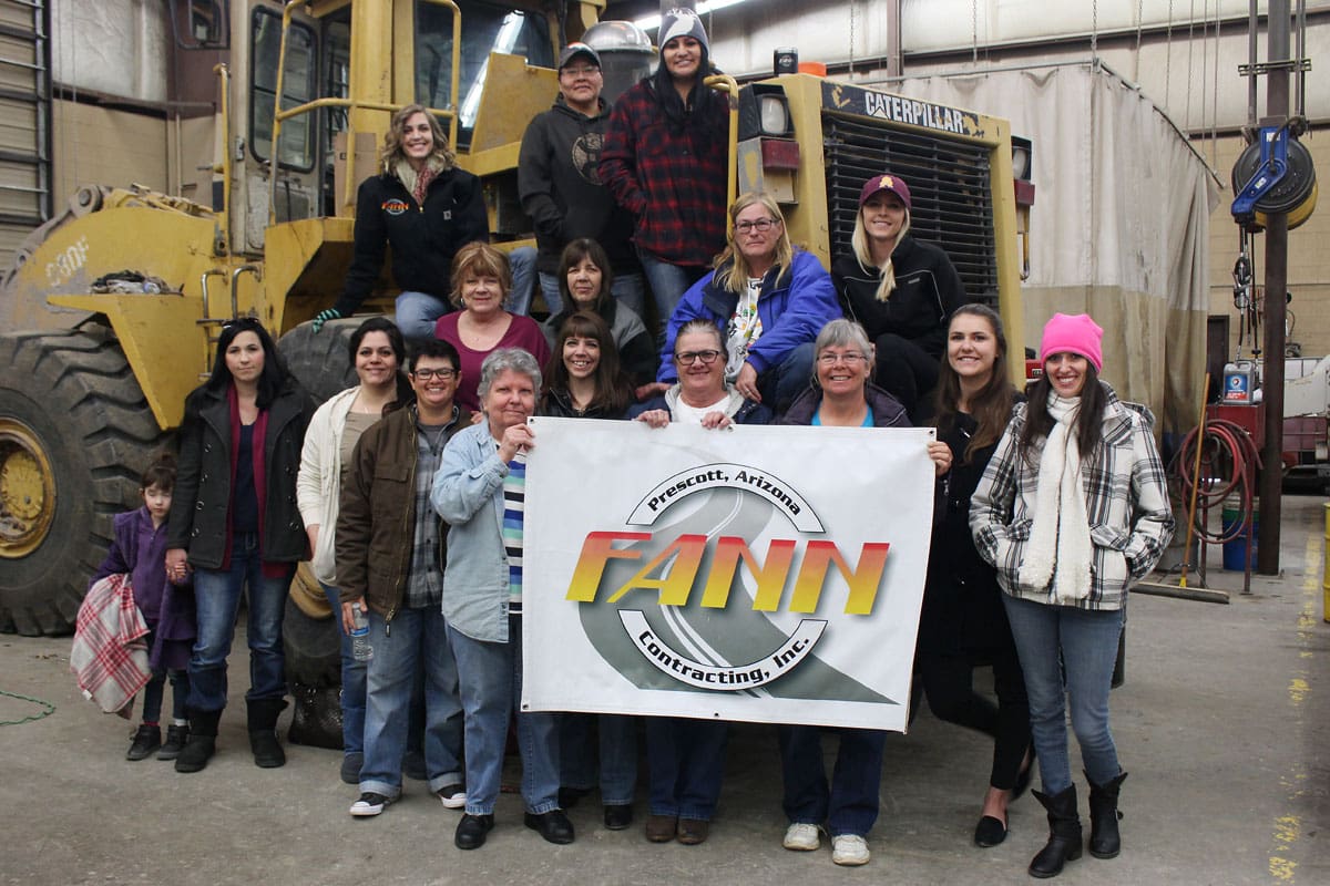 A group of women posing in front of a construction bulldozer.
